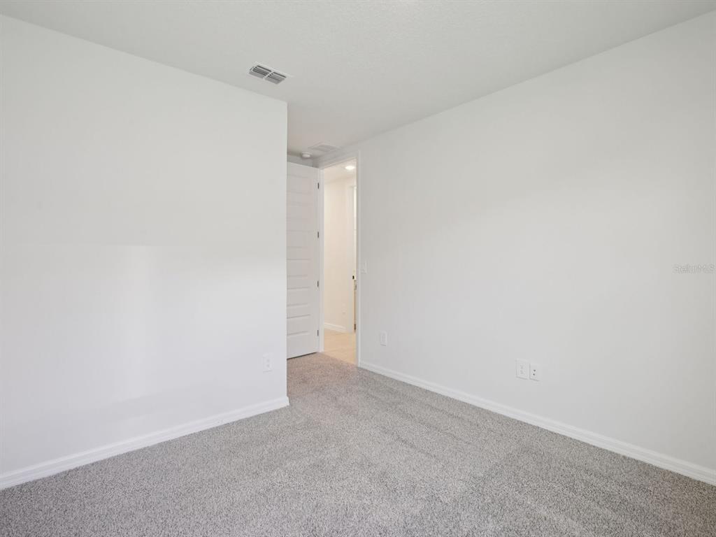 An empty bedroom features white walls, gray carpet, and an open doorway — 11437 STARLING SONG PLACE, PARRISH, FL
