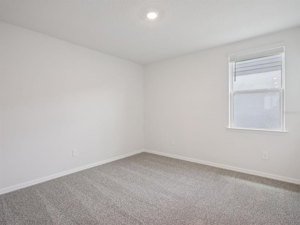An empty bedroom features white walls, gray carpet, and a single window with blinds — 11437 STARLING SONG PLACE, PARRISH, FL