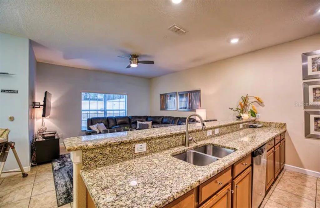 A kitchen with granite countertops and a double sink overlooks a living room with furniture — 2935 BANANA PALM DRIVE, KISSIMMEE, FL