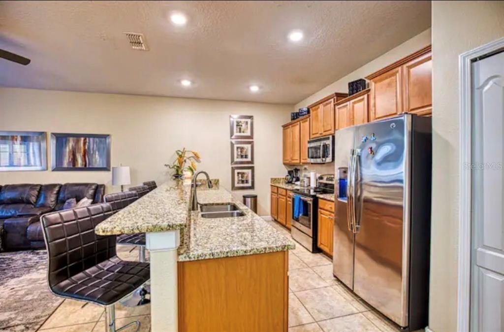 A kitchen with granite countertops, wooden cabinets, stainless steel appliances, and a breakfast bar — 2935 BANANA PALM DRIVE, KISSIMMEE, FL