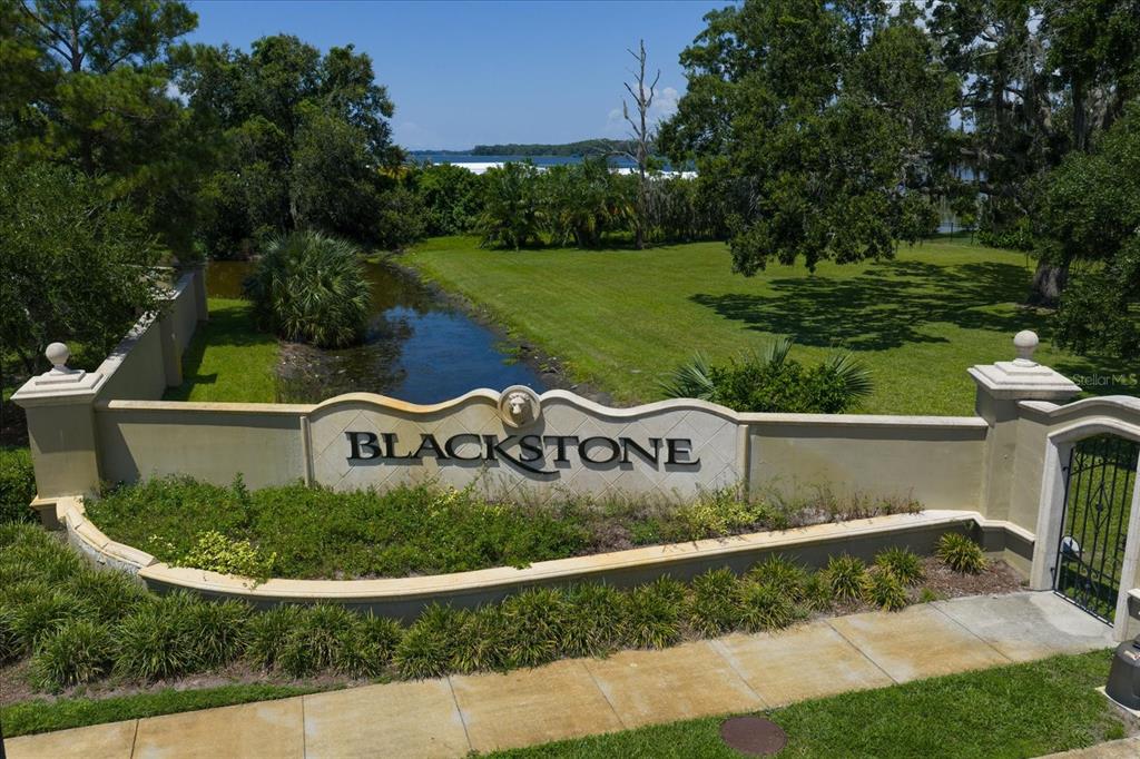 An exterior view of a community entrance sign labeled Blackstone with a pond and trees — 0 BLACKSTONE DRIVE, PALM HARBOR, FL