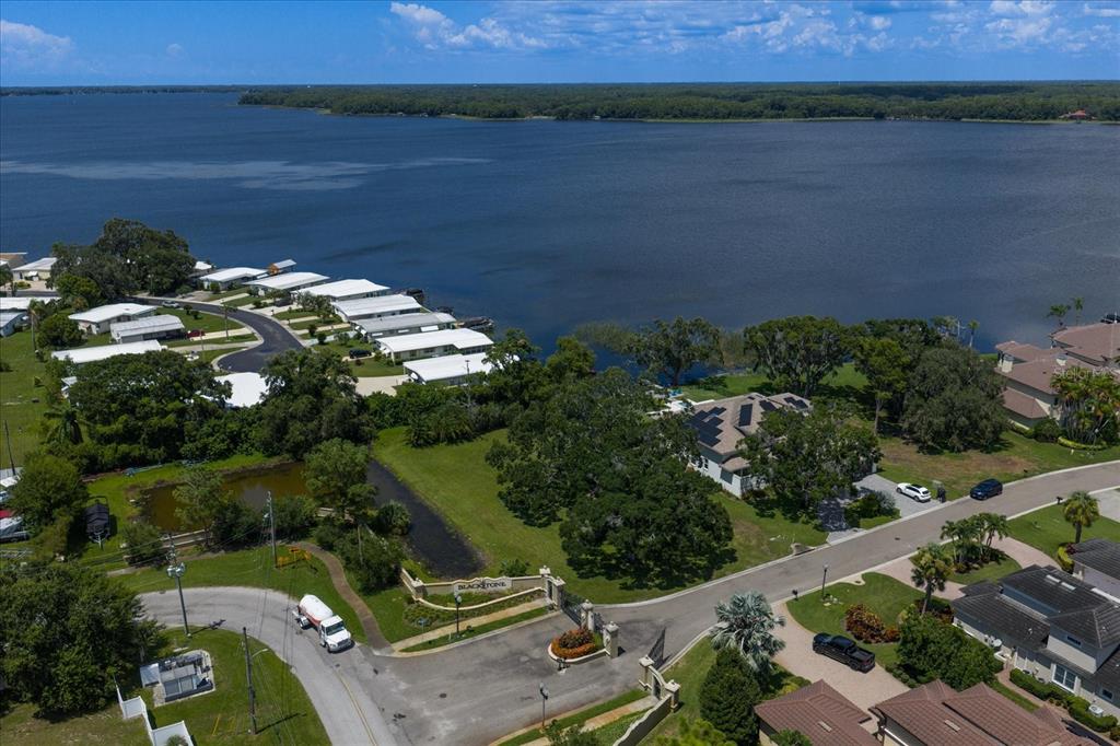 An aerial view shows a gated community entrance, a pond, and houses along a lake — 0 BLACKSTONE DRIVE, PALM HARBOR, FL