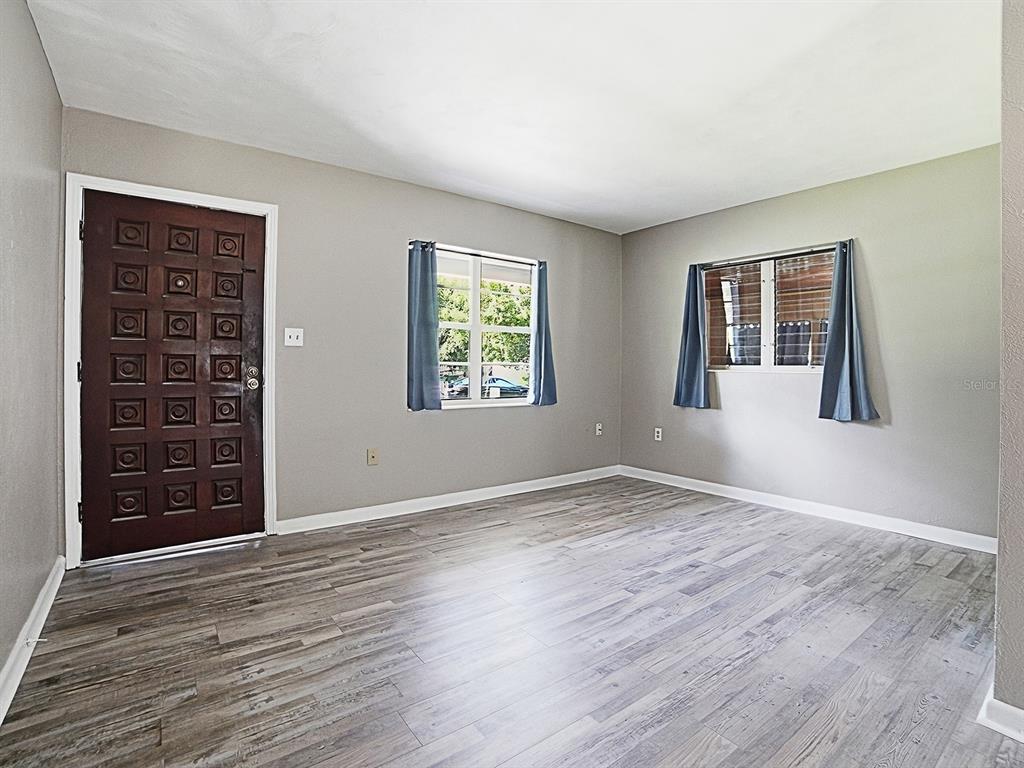 An empty room features gray walls, wood-look flooring, two windows with curtains, and a dark door — 2014 HELMS AVENUE, LEESBURG, FL