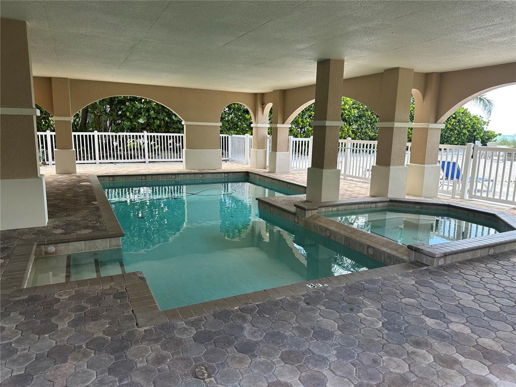 A covered patio features a paver floor, a white fence, and double glass-paneled entry doors — 106 74TH STREET UNIT 100, HOLMES BEACH, FL
