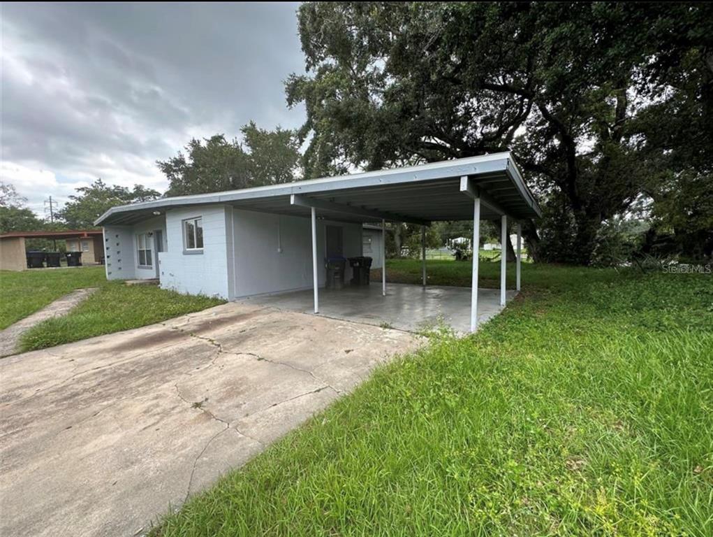 A light-colored single-story house features a concrete driveway and an attached metal carport — 116 JUPITER CIRCLE, ORLANDO, FL