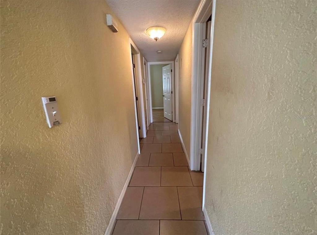 A hallway with tan walls, tiled flooring, and multiple doorways leading to other rooms — 116 JUPITER CIRCLE, ORLANDO, FL