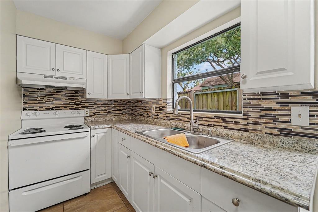 A kitchen with white cabinets, granite countertops, a tiled backsplash, and a stainless steel sink — 12310 TOUCHTON DRIVE UNIT 43, TAMPA, FL