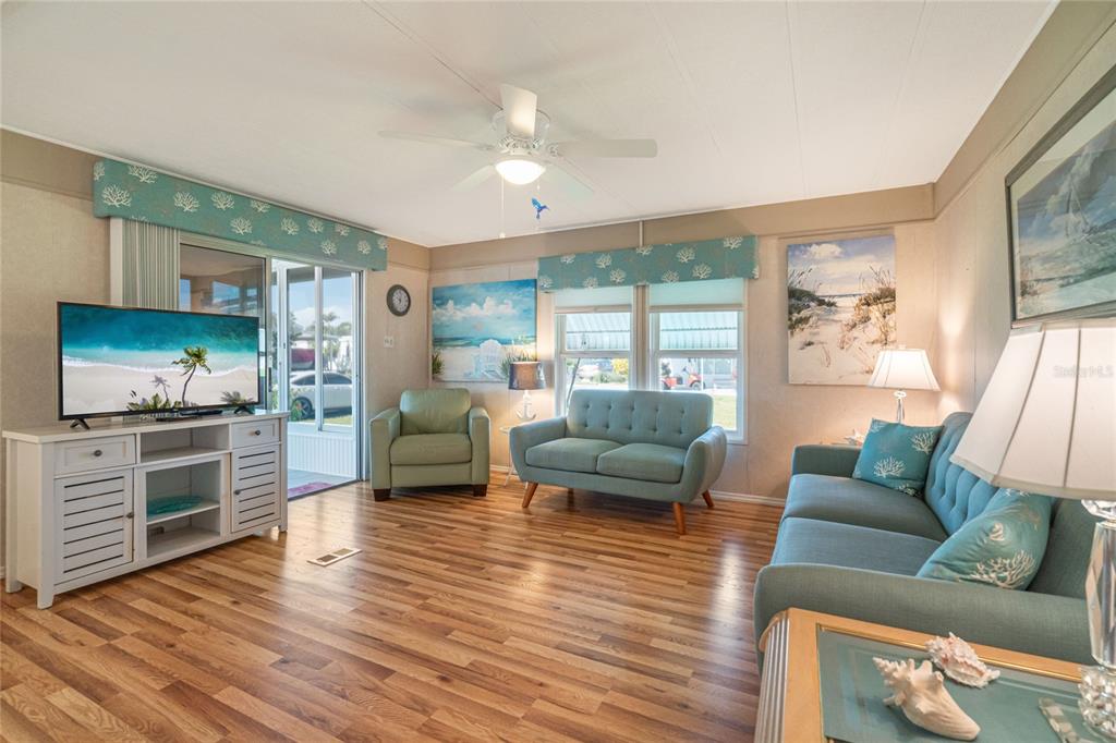 A living room features wood-look flooring, a ceiling fan, and coastal-themed furniture and decor — 700 FAIRMOUNT DRIVE, NORTH PORT, FL
