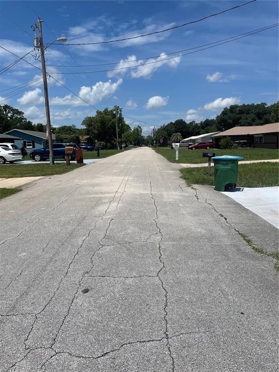 A paved residential street with cracked asphalt, utility poles, and houses on both sides — 210 LAKEWOOD DRIVE, DEBARY, FL