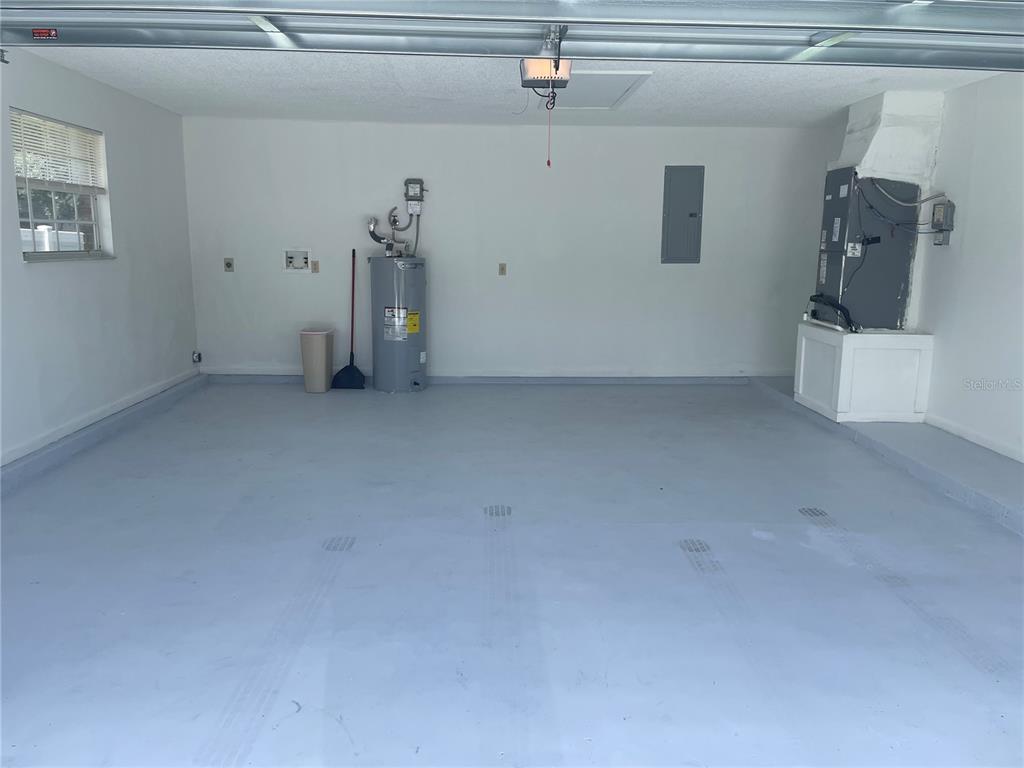 An empty garage features a painted concrete floor, a water heater, and an HVAC unit — 210 LAKEWOOD DRIVE, DEBARY, FL