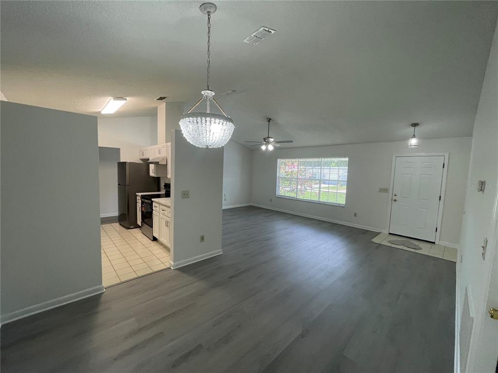 An open-concept living area with grey wood-look flooring, a crystal chandelier, and an adjacent kitchen — 210 LAKEWOOD DRIVE, DEBARY, FL