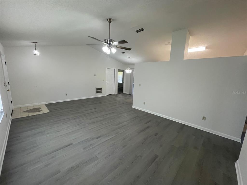 An empty living room features gray wood-look flooring, vaulted ceilings, and a ceiling fan — 210 LAKEWOOD DRIVE, DEBARY, FL