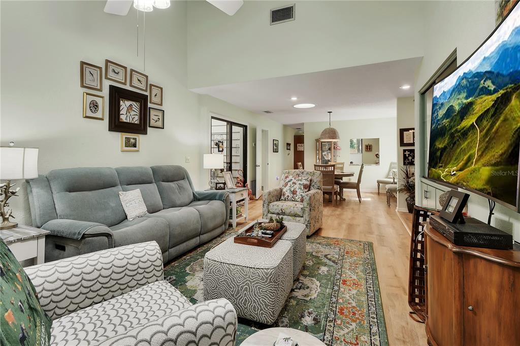 A living room with a vaulted ceiling, a grey sofa, patterned armchairs, and a dining area — 904 VILLAGE GREEN ROAD UNIT 3, DELAND, FL