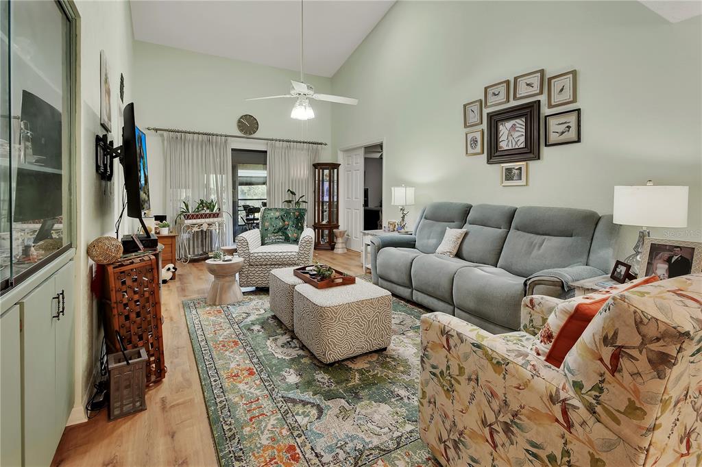 A living room features a vaulted ceiling, a gray sofa, patterned ottomans, and a rug — 904 VILLAGE GREEN ROAD UNIT 3, DELAND, FL