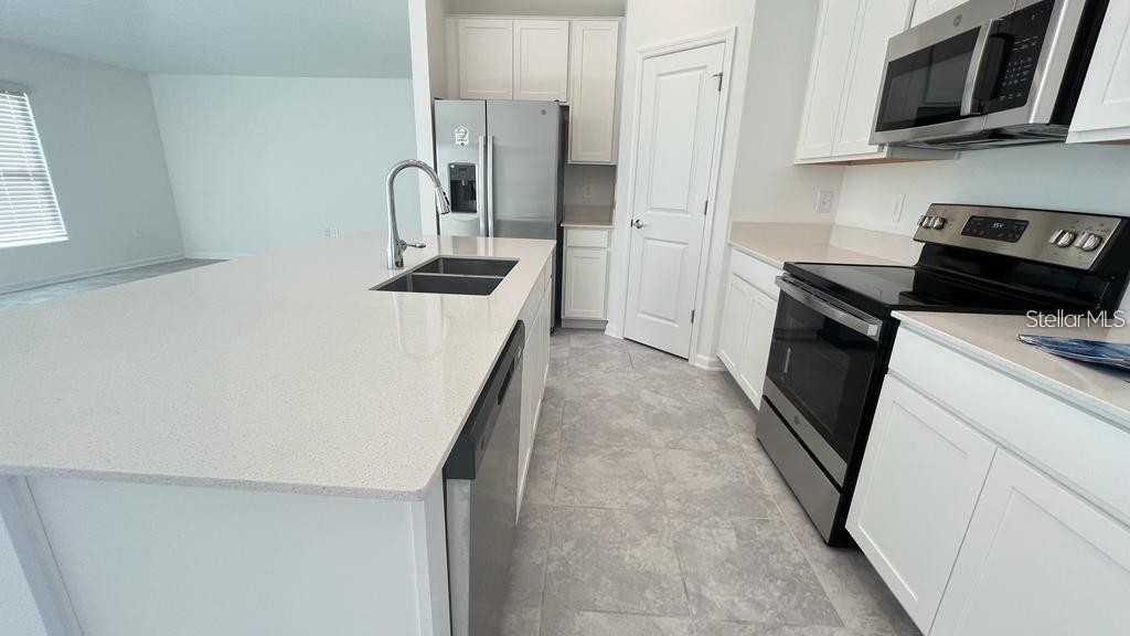 A modern kitchen features white cabinets, stainless steel appliances, and a large quartz-topped island — 263 BRAVE ROAD, DAVENPORT, FL