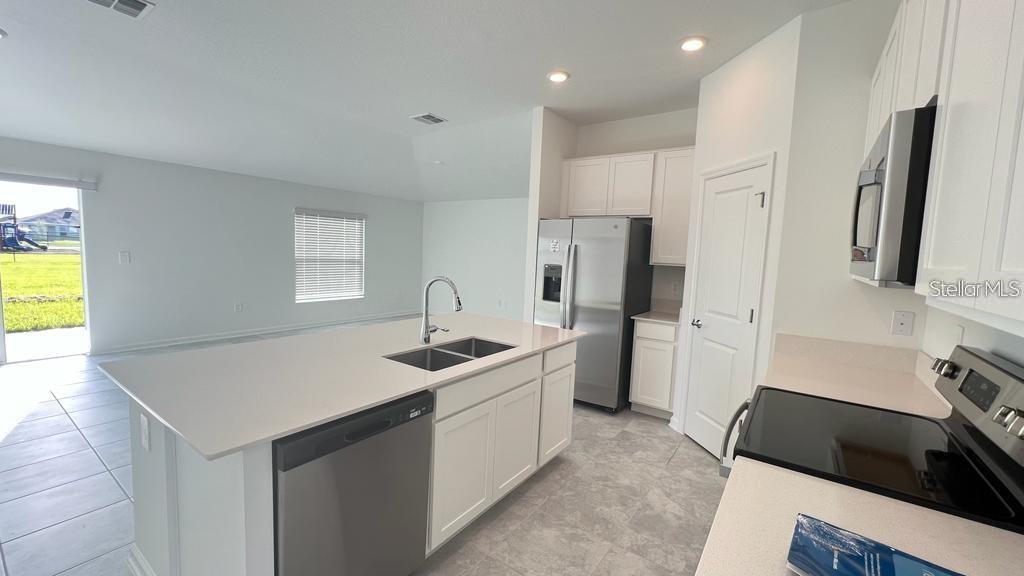 A modern kitchen features white cabinets, stainless steel appliances, and a central island with sink — 263 BRAVE ROAD, DAVENPORT, FL