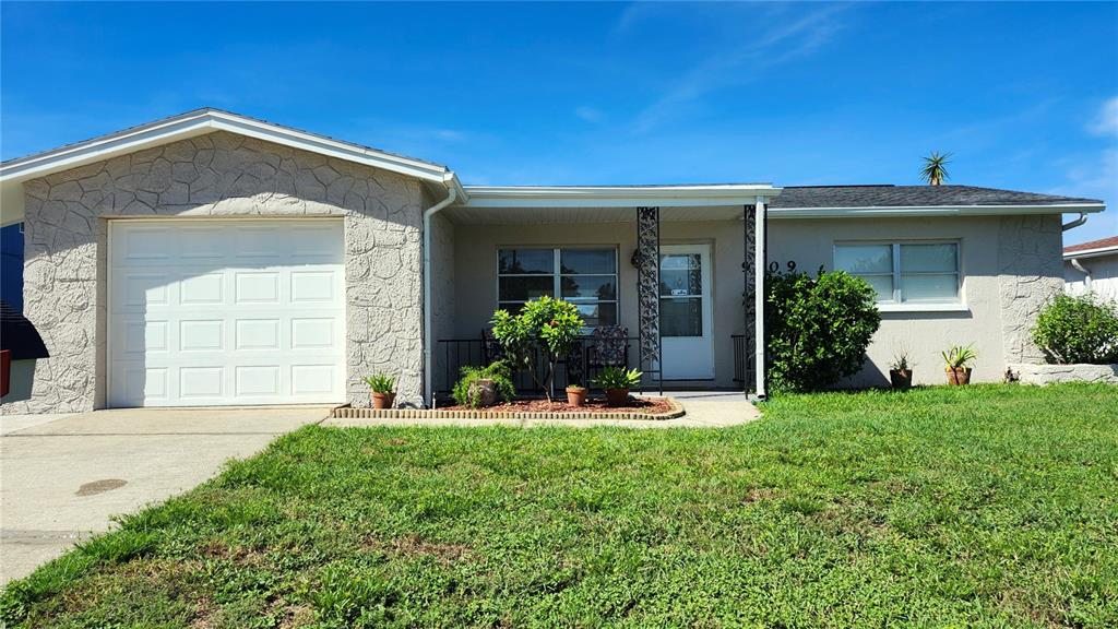 A house exterior features a covered porch with two chairs, a small table, and landscaping — 9709 LAKESIDE LANE, PORT RICHEY, FL