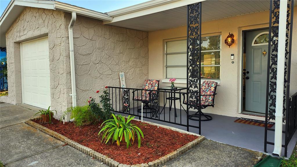 A house exterior features a covered porch with two chairs, a small table, and landscaping — 9709 LAKESIDE LANE, PORT RICHEY, FL