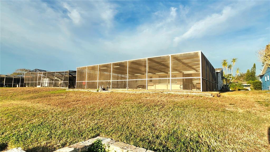 A large screened-in pool enclosure sits on a grassy lot behind a residential house — 9709 LAKESIDE LANE, PORT RICHEY, FL
