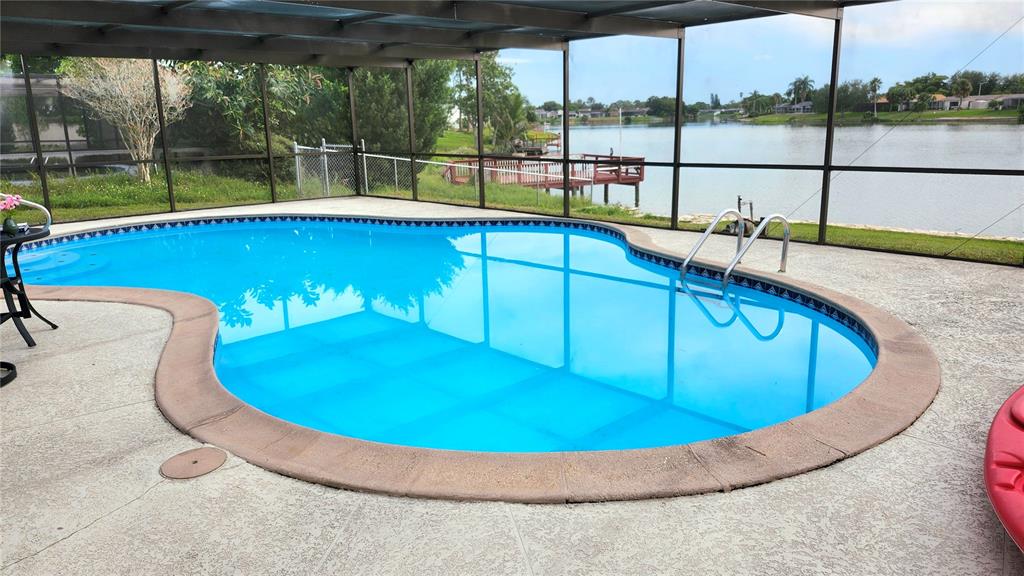 A stone patio overlooks a lake with houses along the distant shoreline — 9709 LAKESIDE LANE, PORT RICHEY, FL