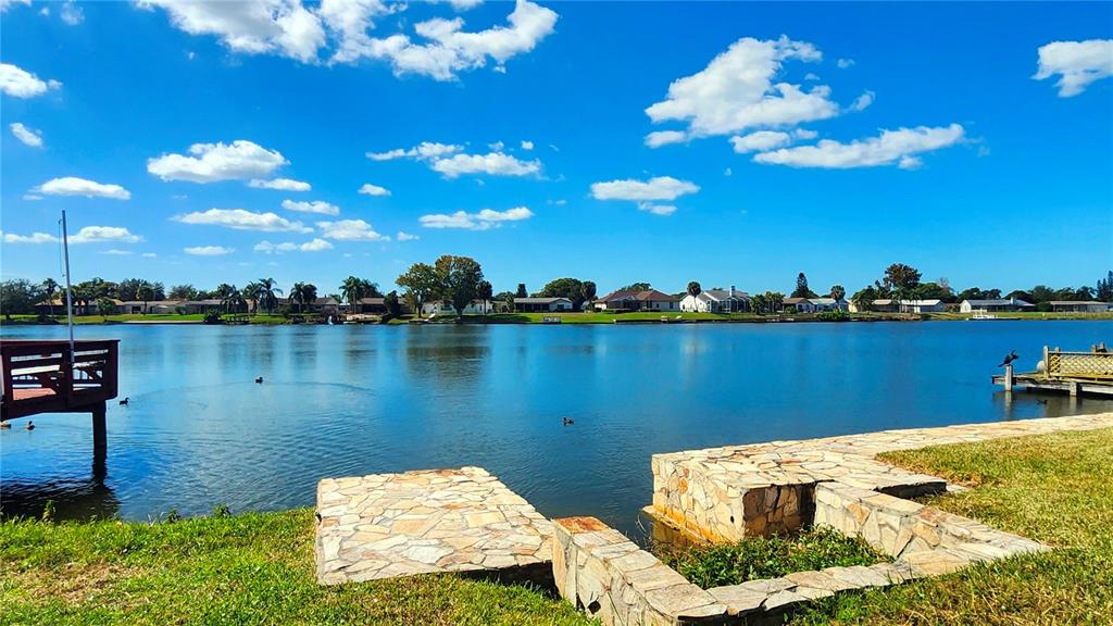A stone patio overlooks a lake with houses along the distant shoreline — 9709 LAKESIDE LANE, PORT RICHEY, FL