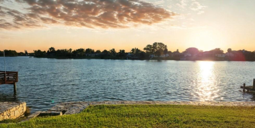 A grassy lawn overlooks a lake with two wooden docks at sunset — 9709 LAKESIDE LANE, PORT RICHEY, FL
