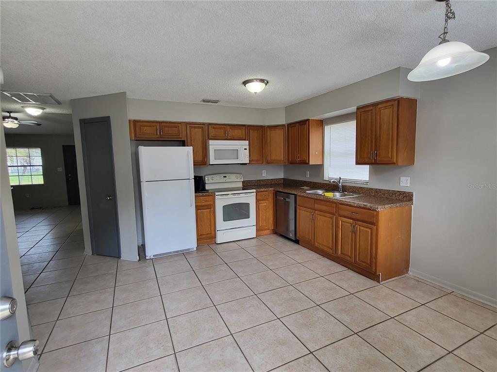 A kitchen features wood cabinets, white appliances, granite countertops, and light-colored tile flooring — 787 LINCOLN PARKWAY, OVIEDO, FL