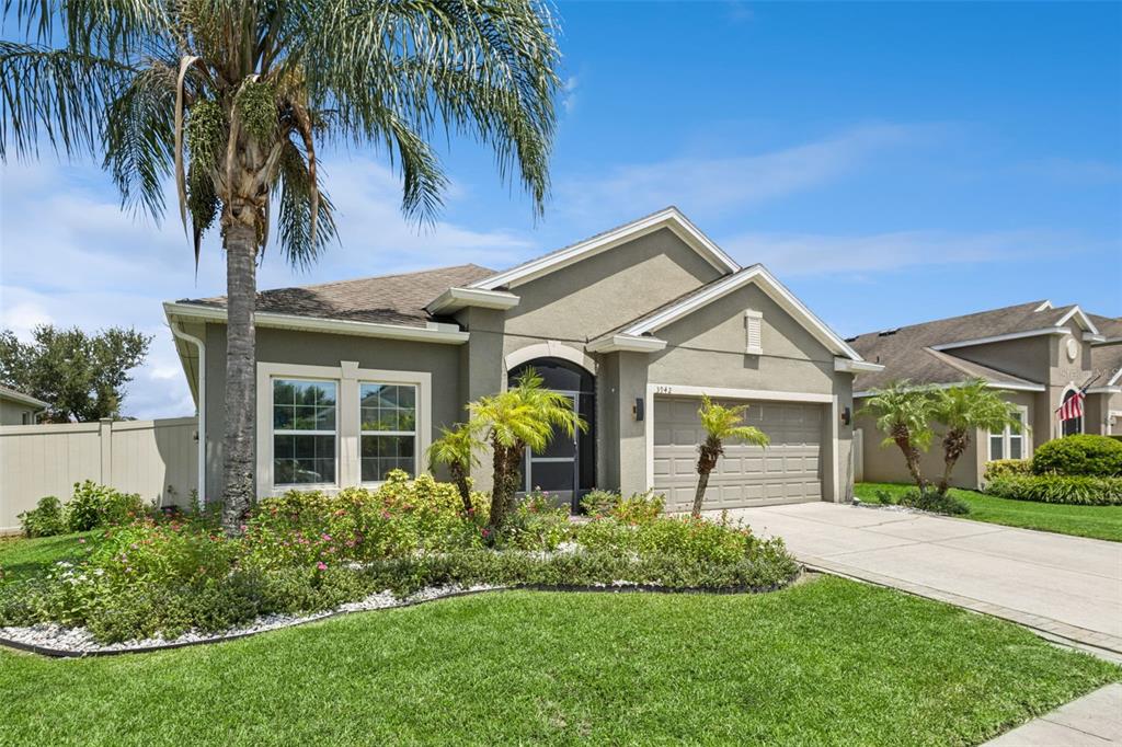 A single-story suburban house with a tan stucco exterior, a two-car garage, and palm trees — 3942 ETERNITY CIRCLE, ST CLOUD, FL