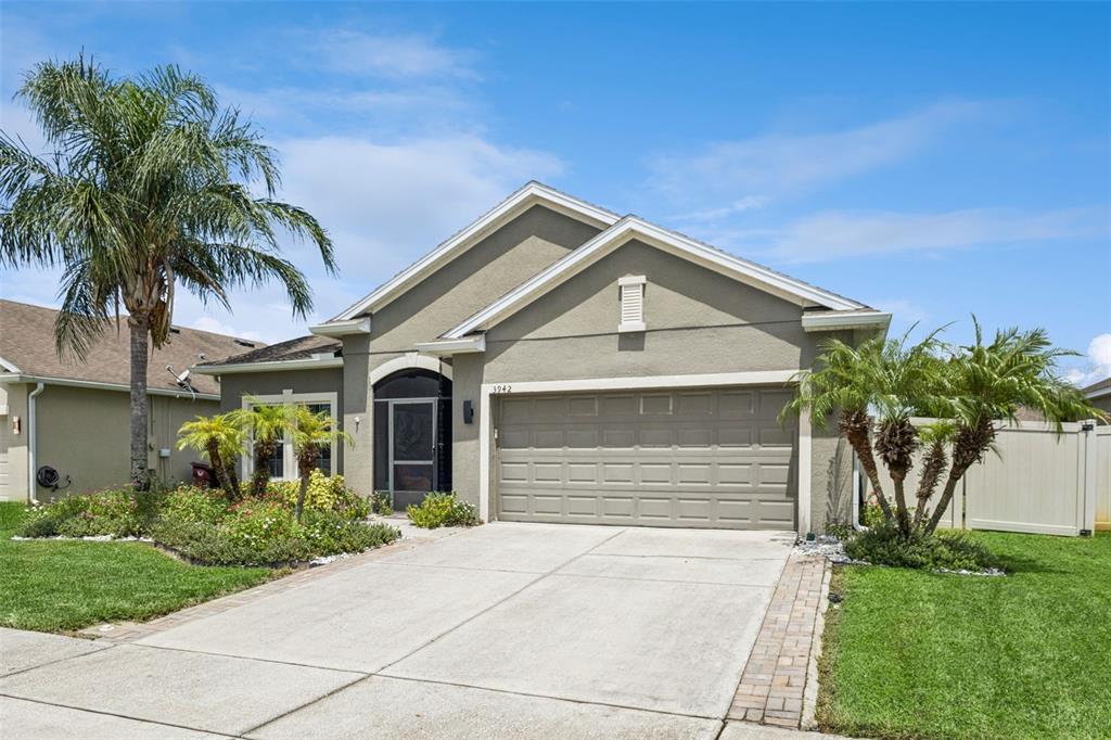 A single-story house with a beige stucco exterior, a two-car garage, and a palm tree — 3942 ETERNITY CIRCLE, ST CLOUD, FL