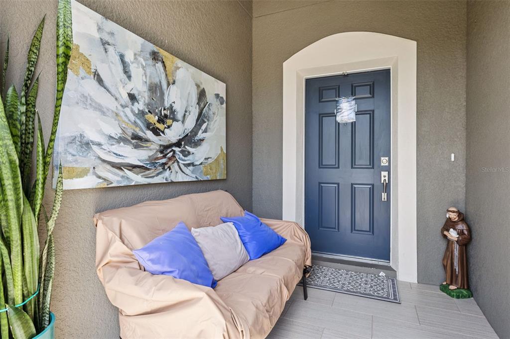 A covered entryway features a blue front door, a futon with pillows, and a potted plant — 3942 ETERNITY CIRCLE, ST CLOUD, FL
