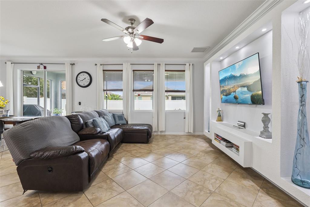 A living room features a brown leather sectional, tile flooring, and a wall-mounted television — 3942 ETERNITY CIRCLE, ST CLOUD, FL