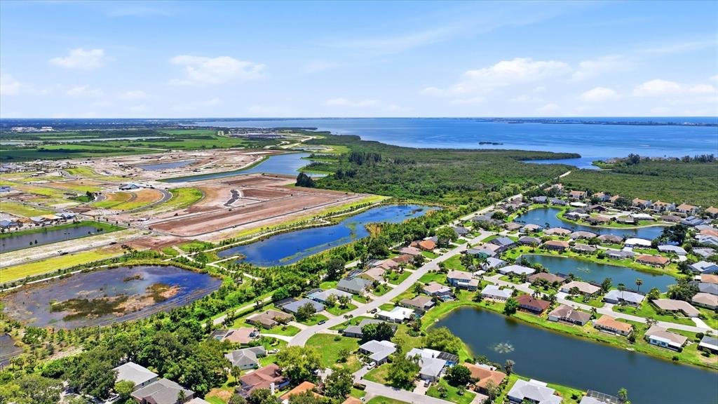 An aerial view shows a suburban neighborhood with houses, ponds, and nearby undeveloped land — 5015 86TH STREET COURT W, BRADENTON, FL