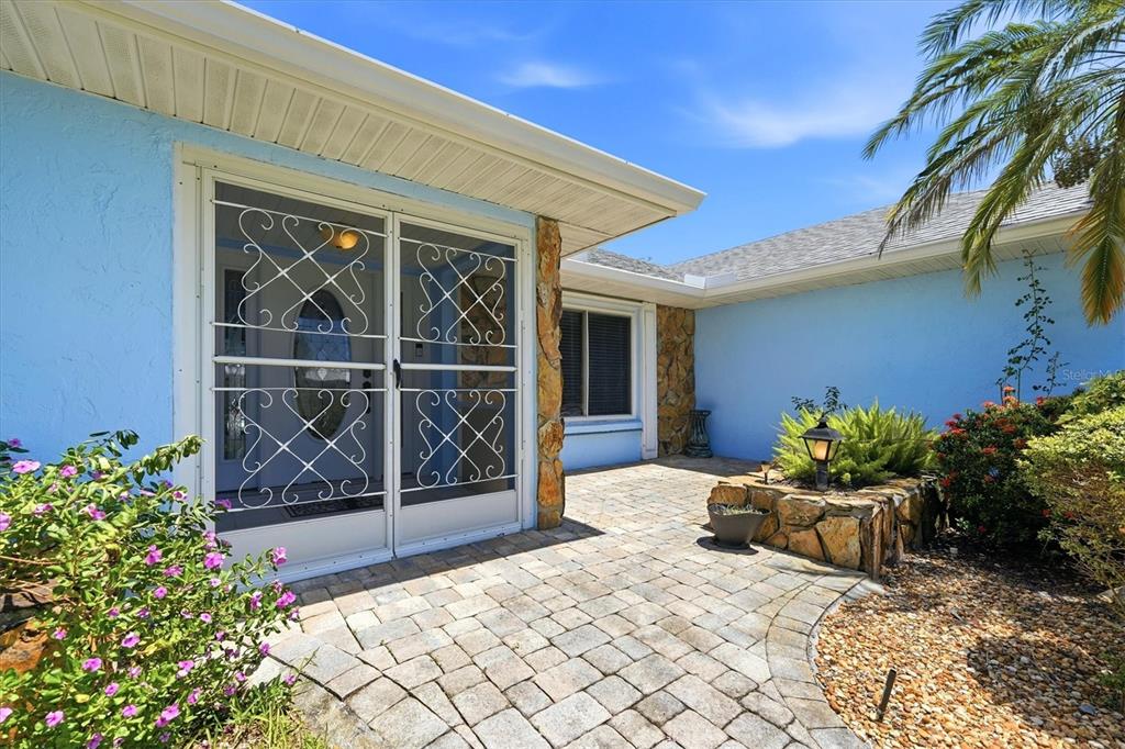 A blue house exterior features a stone-accented entryway, a paved patio, and a screen door — 5015 86TH STREET COURT W, BRADENTON, FL