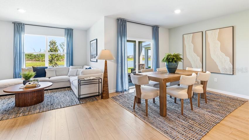 A bright living and dining area features light wood floors, blue curtains, and neutral furniture — 17140 LEGACY PRESERVE DRIVE, PARRISH, FL