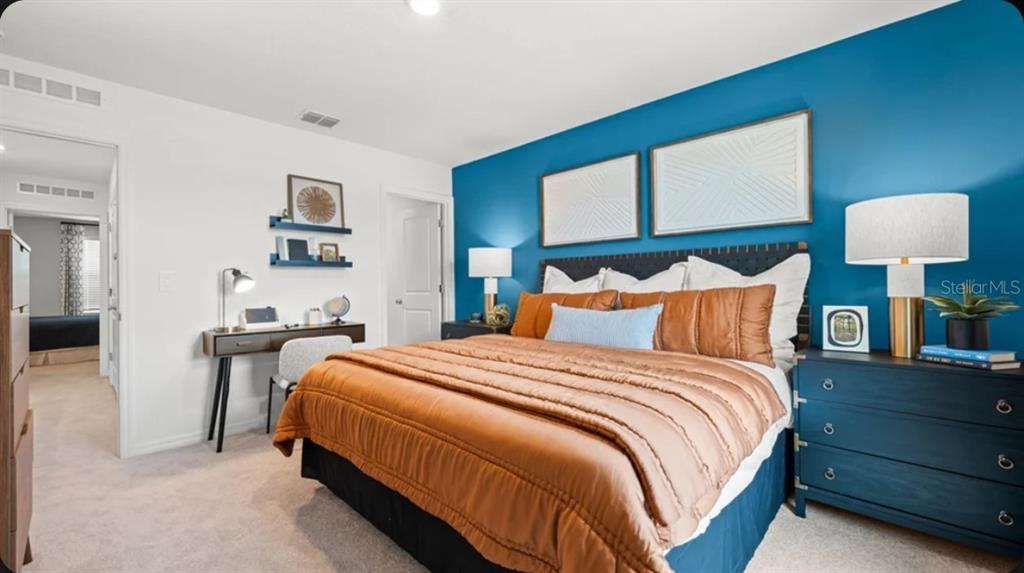A bedroom features a blue accent wall, a bed with orange bedding, and a desk — 675 NESS ISLAND DRIVE UNIT 0, MOUNT DORA, FL