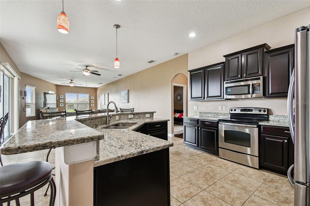 A kitchen with dark cabinets, granite countertops, stainless steel appliances, and an island with seating — 205 ORANGE MILL AVE, RUSKIN, FL