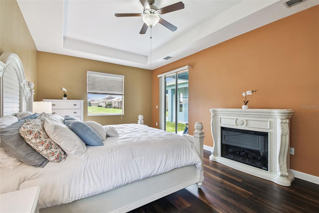 A bedroom features a white bed, a fireplace, dark wood floors, and a tray ceiling — 205 ORANGE MILL AVE, RUSKIN, FL