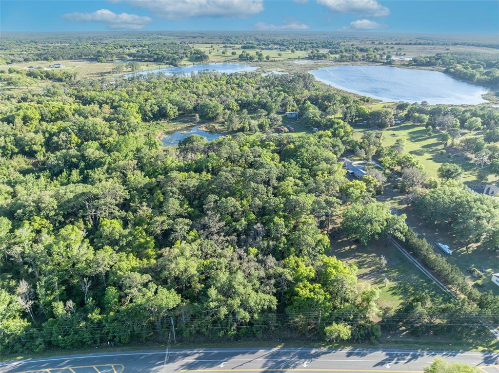An aerial view shows a wooded lot bordering a road with a lake in the background — TBD COUNTY ROAD 48, YALAHA, FL
