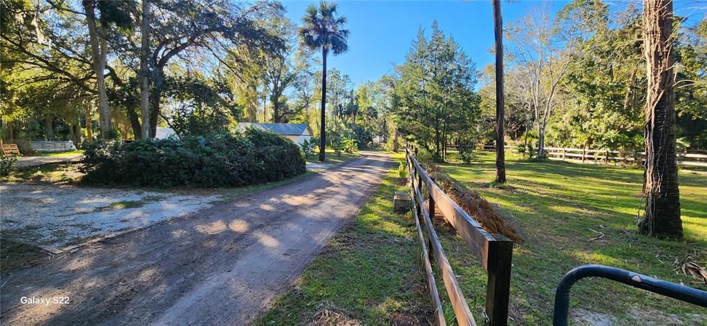 A dirt driveway leads past a wooden fence toward a house surrounded by trees — 680 E BLACK POINT ROAD, BUNNELL, FL