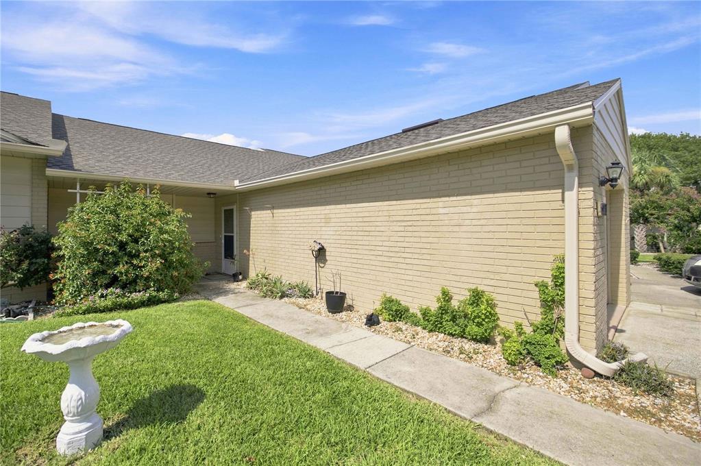 A tan brick house exterior features a concrete walkway, a birdbath, and green landscaping — 5033 SE 109TH PLACE, BELLEVIEW, FL