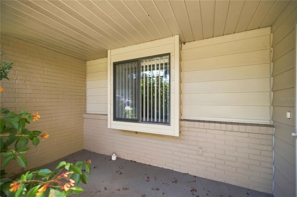 A covered porch features a brick wall, horizontal siding, and a single window with blinds — 5033 SE 109TH PLACE, BELLEVIEW, FL