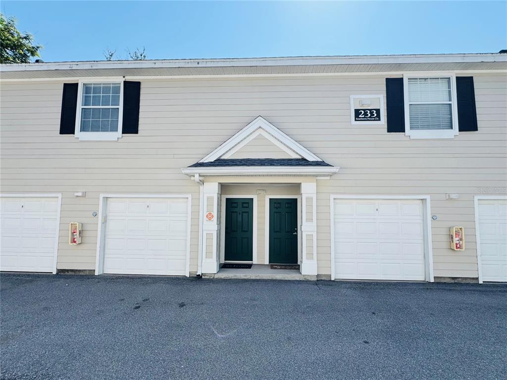 The exterior of a two-story building features light siding, two garage doors, and two front doors — 233 SOUTHERN PECAN CIRCLE UNIT 101, WINTER GARDEN, FL