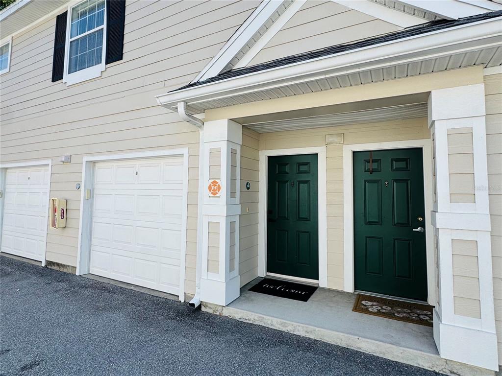 The exterior of a two-story building features two garage doors and two dark green entry doors — 233 SOUTHERN PECAN CIRCLE UNIT 101, WINTER GARDEN, FL
