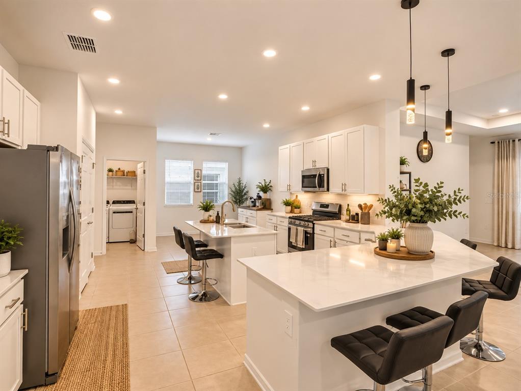 A modern white kitchen features a large island, stainless steel appliances, and black bar stools — 2155 RIDER RAIN LANE, APOPKA, FL