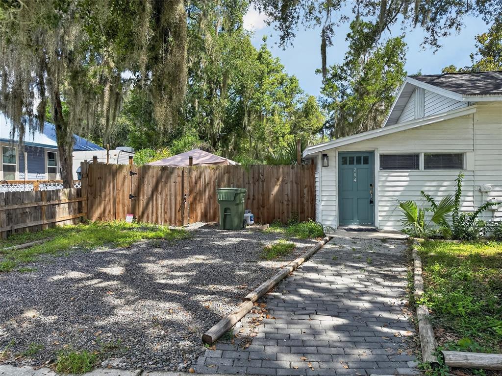 A gravel driveway leads to a white house with a teal door and brick walkway — 325 S 2ND STREET, LEESBURG, FL