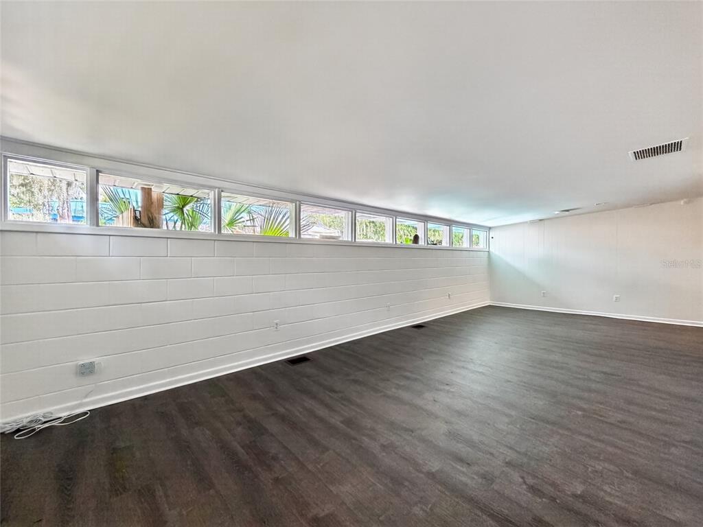 A room with dark wood-look flooring, white block walls, and a row of clerestory windows — 325 S 2ND STREET, LEESBURG, FL