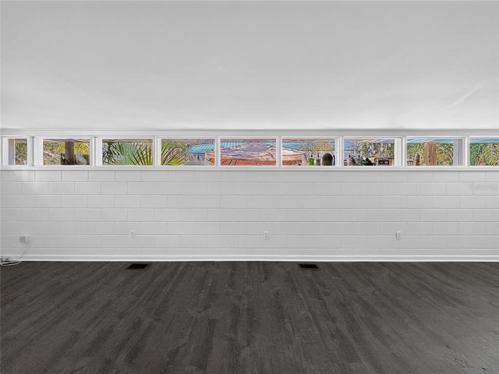 A room with dark wood-look flooring, a white cinder block wall, and a row of windows — 325 S 2ND STREET, LEESBURG, FL