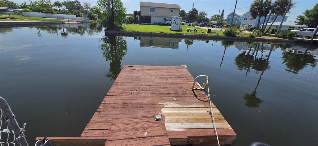 A wooden dock extends into a calm canal with houses visible on the opposite bank — 13324 CAROL DRIVE, HUDSON, FL