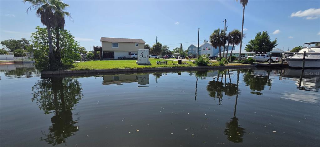 A waterfront view of a grassy yard with a house, palm trees, and a boat — 13324 CAROL DRIVE, HUDSON, FL