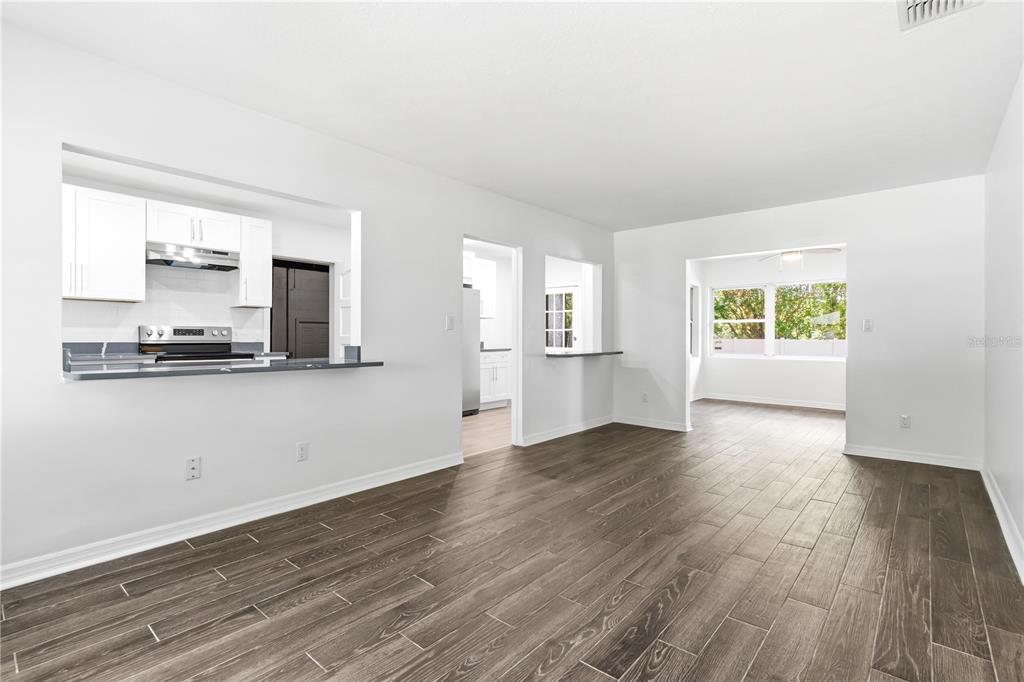 A bright living area with wood-look tile flooring, white walls, and a kitchen pass-through window — 10 S ORION AVENUE, CLEARWATER, FL